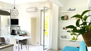 Un salon moderne avec un canapé bleu, un coin cuisine doté d’une table à manger et une grande fenêtre avec des rideaux.