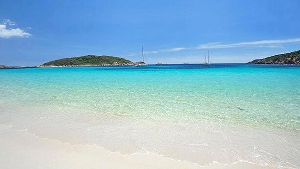 A beach with clear turquoise water, sandy shore, and distant green hills. - Beach house with private beach access  (Perd'e Sali)