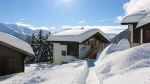 Una cabaña de montaña cubierta de nieve con fachada de madera, una escalera visible y un letrero con el nombre y la información de contacto.