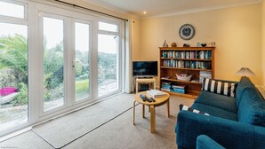 A living room with a large window, a bookshelf, a sofa, and a television. - Sea Grove -  a bungalow that sleeps 7 guests  in 3 bedrooms (Ventnor)