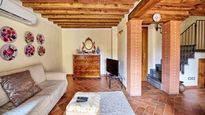 A living room with a wooden ceiling, a sofa, a TV, and a fireplace. - Flavia 3 - Vacation Rental with swimming pool in Lucca (Lucca)