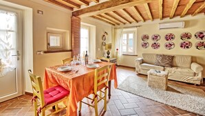 A dining area with a wooden ceiling, a table set for four, and a sofa in the adjacent living room. - Flavia 3 - Vacation Rental with swimming pool in Lucca (Lucca)