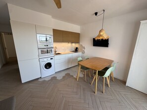 Una cocina moderna con electrodomésticos integrados, una zona de comedor con mesa y sillas de madera, y una lámpara colgante.