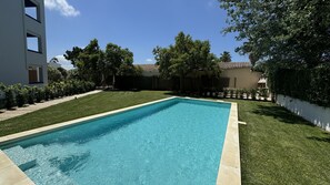 Una piscina rectangular de agua azul cristalina, rodeada de césped y árboles bien cuidados.