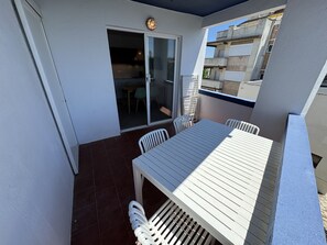 Un balcón con mesa y sillas, una puerta corredera de vidrio y vistas a edificios cercanos.