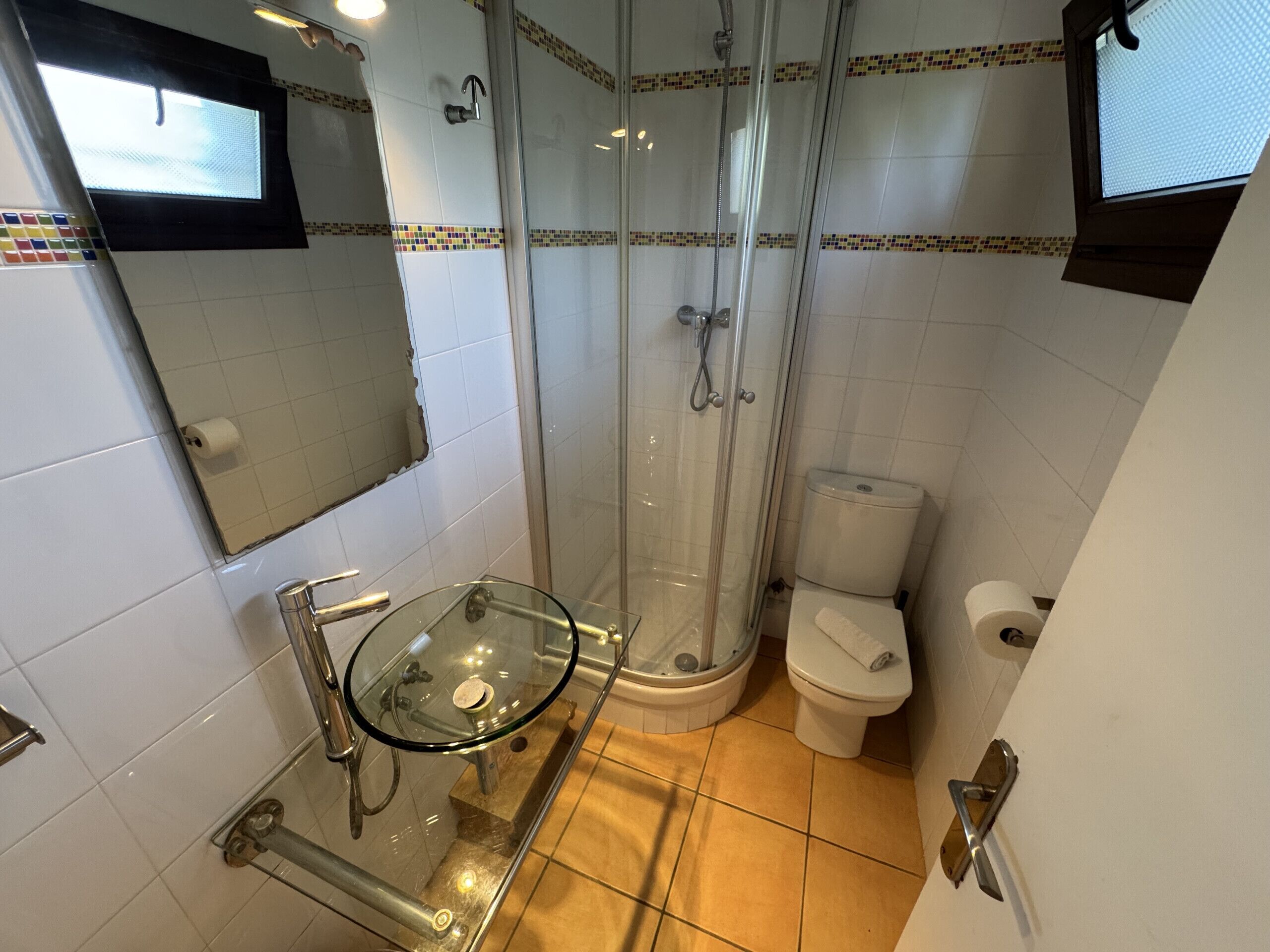 Un baño con ducha envuelta en vidrio, un lavabo de vidrio, un inodoro y un espejo.