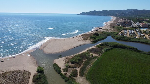 Vue aérienne d’une zone côtière comprenant une plage, une rivière et un quartier résidentiel avec des bâtiments.