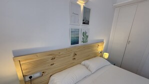 Une chambre à coucher avec une tête de lit en bois, un lit recouvert de draps blancs, une table de chevet avec une lampe et des tableaux encadrés accrochés au mur.