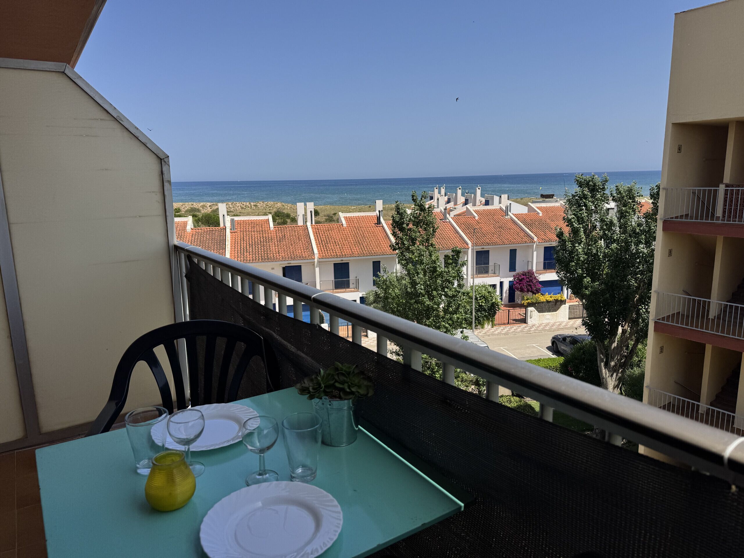 Een balkon met een eettafel, met uitzicht op een kustgebied met gebouwen en de zee.