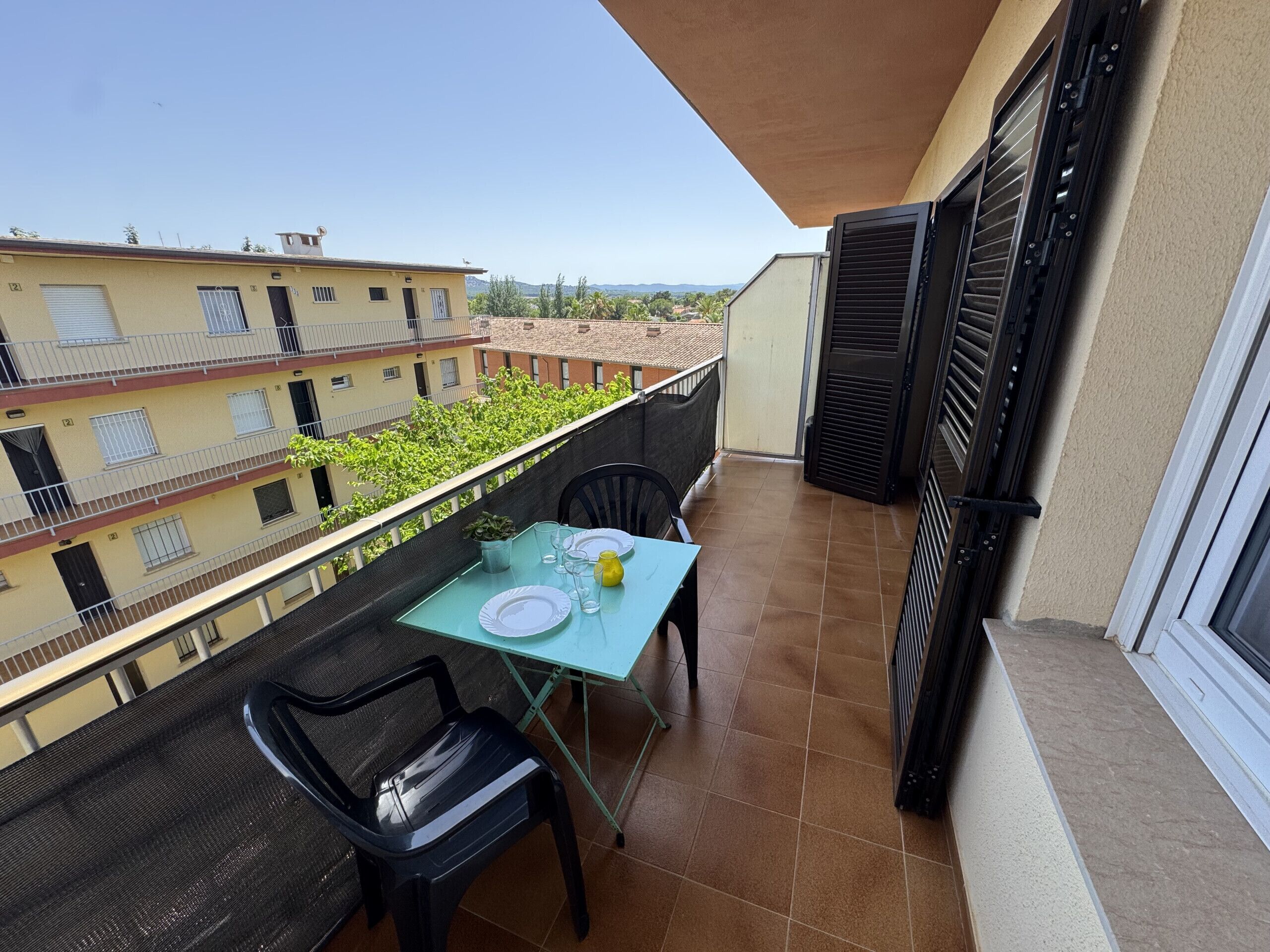 A balcony with a table set for two, chairs, and a view of neighboring buildings.