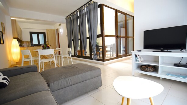 A modern living room with a grey sofa, a white coffee table, and a TV on a white stand.