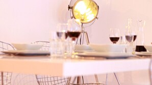 Ein Esstisch ist mit Tellern, Gläsern und einer Weinflasche gedeckt, beleuchtet von einer Lampe im Vintage-Stil.