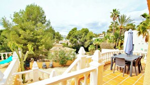 A terrace with a table and chairs, surrounded by a white balustrade, overlooking a garden with trees and a building in the background. - Sofia - holiday home with private swimming pool in Moraira (Teulada)