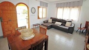A living room with a brown leather sofa, a wooden dining table with chairs, and a large window with curtains. - Sofia - holiday home with private swimming pool in Moraira (Teulada)