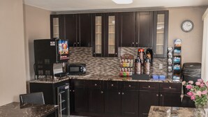 A compact kitchen with dark wood cabinets, a microwave, a coffee maker, and a dining area with a table and chairs.