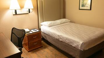 Quarto de hotel com uma cama, uma escrivaninha com cadeira, mesa de cabeceira, duas luminárias fixadas na parede e um quadro enquadrado na parede.
