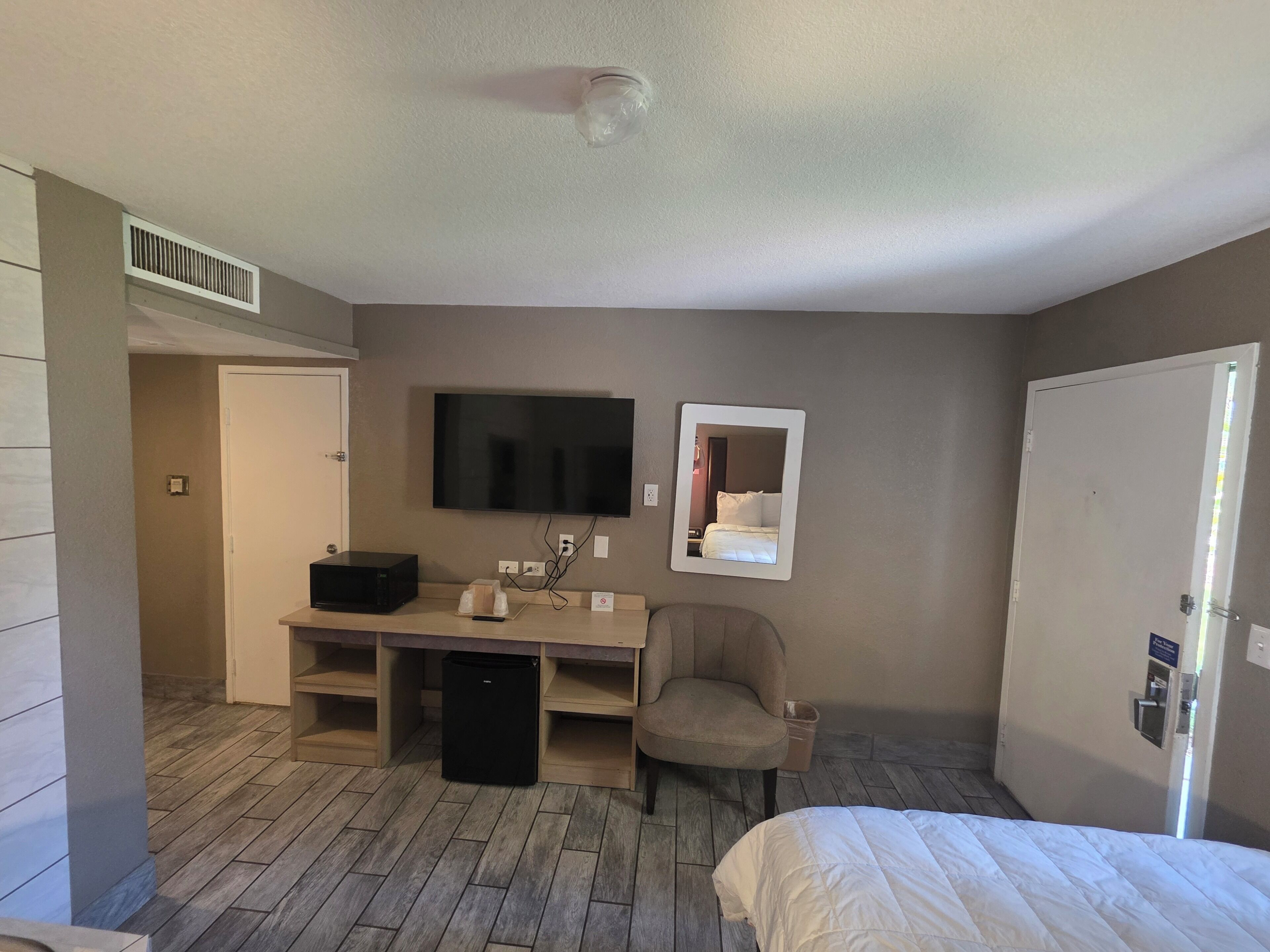 A room with a bed, a desk with a computer, a chair, a TV, and a mirror.