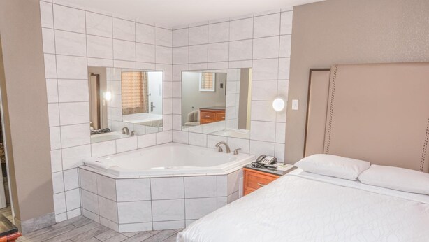 A modern hotel room with a large bed, a separate bathroom with a bathtub, and two mirrors.
