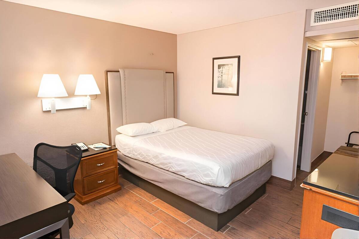 Une chambre d’hôtel comprenant un lit, une table de chevet, un bureau, une chaise et des lampes fixées au mur.