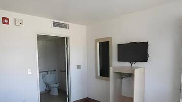 A hotel room with a toilet, a sink, a mirror, and a television.