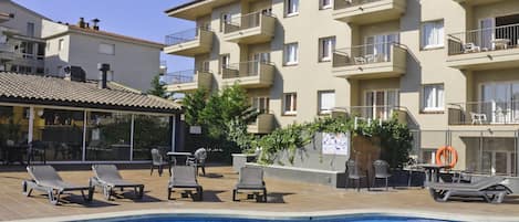 A swimming pool with lounge chairs, a bar area, and a building with balconies.