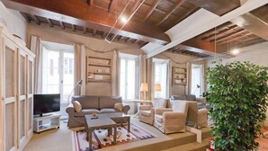 Una sala de estar con sofá, sillones, una mesa de centro, televisor y una planta grande.