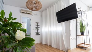 A modern living room with a large flat-screen TV, a wicker ceiling light, and a potted plant. - San Francisco Penthouse Studio (Sevilla)