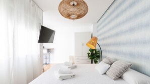 A modern bedroom with a large bed, a flat-screen TV, a wicker ceiling light, and a bedside table with a lamp. - San Francisco Penthouse Studio (Sevilla)