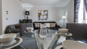 A modern living room with a glass-top coffee table, two sofas, and a painting on the wall.