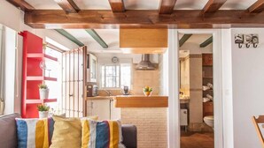 Un salón acogedor con sofá, cojines de colores, una zona de cocina con encimera de madera y un reloj a la vista.