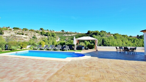 A swimming pool with lounge chairs and a pergola, surrounded by a patio area with a view of a hilly landscape. - Finca La Verema - holiday home with private swimming pool in Benissa (Benissa)