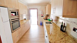 A kitchen with wooden cabinets, stainless steel appliances, a granite countertop, and a view to the dining area. - Finca La Verema - holiday home with private swimming pool in Benissa (Benissa)