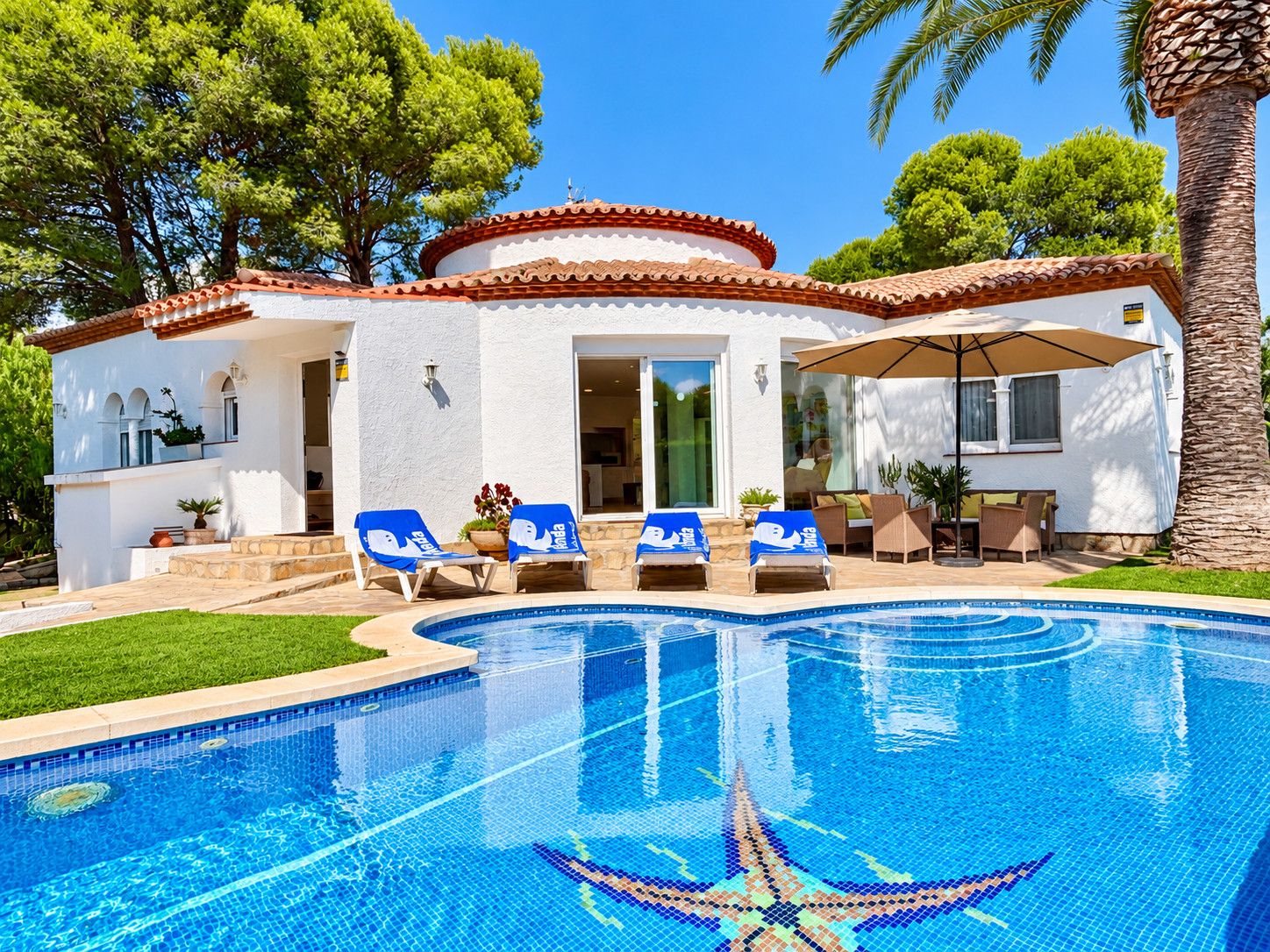 A poolside area with a clear blue pool, lounge chairs, and a covered patio.