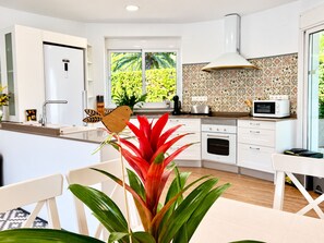 A modern kitchen with white cabinetry, a built-in oven, a microwave, and a window with a view of greenery.