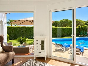 A room with a view of a swimming pool, a sofa, a cabinet, and a patterned rug.