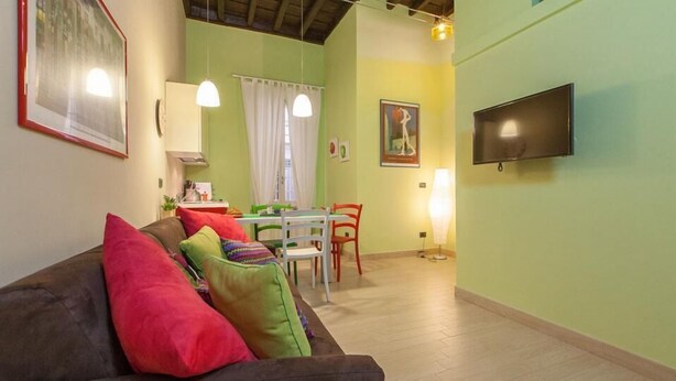Una sala de estar acogedora con un sofá, una mesa de comedor y sillas. Un televisor de pantalla plana está montado en la pared.