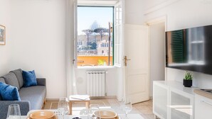 A modern living room with a dining area, a sofa, a TV, and a window with a view of buildings. - Your own private view over St.Peter! (Rome)