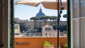 A balcony with a view of a dome and trees, a table with a glass, and a potted plant. - Your own private view over St.Peter! (Rome)