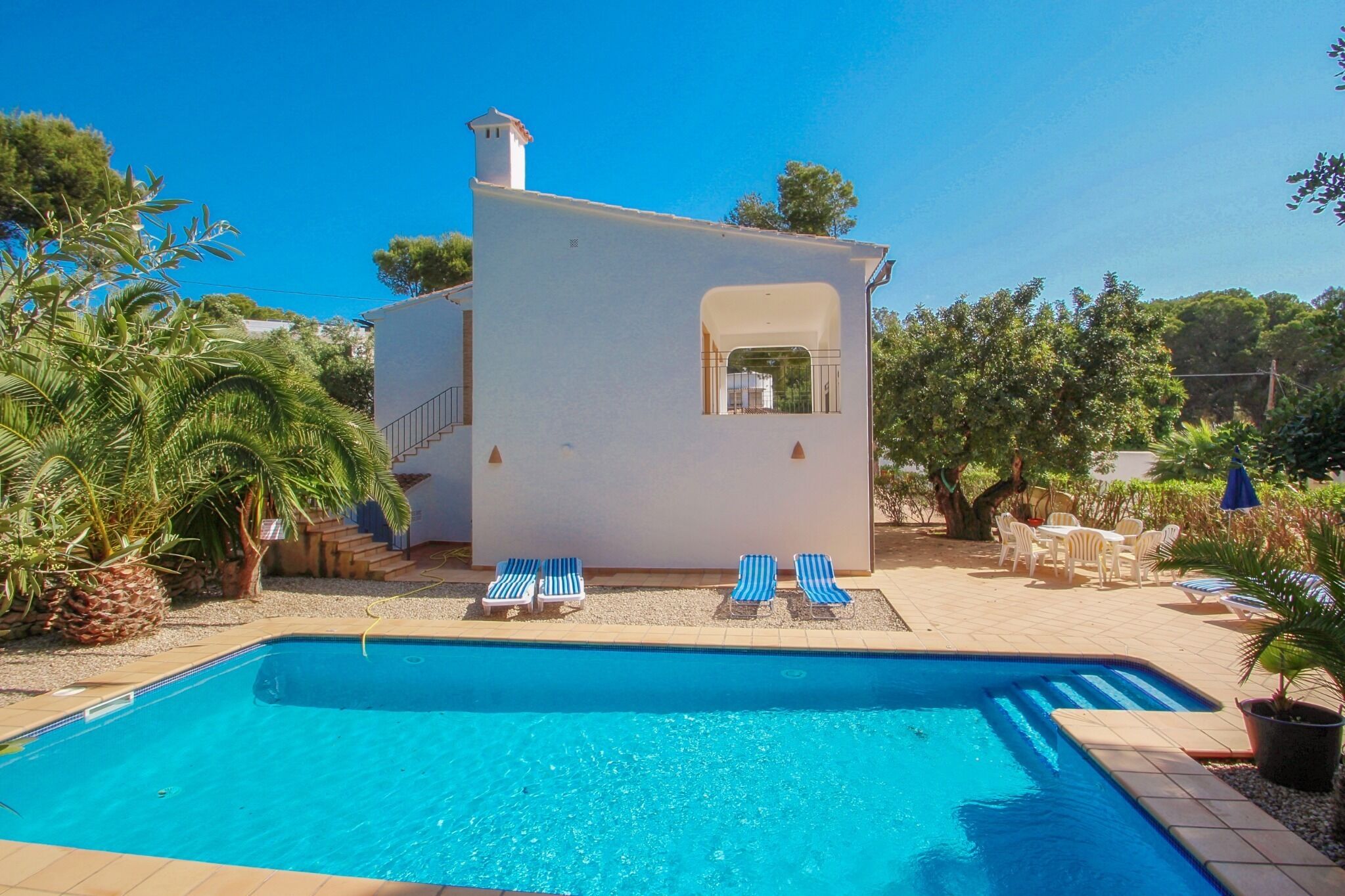 Área de piscina com um pequeno edifício, espreguiçadeiras e uma piscina.