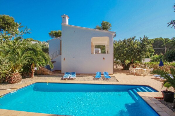 Un espace aménagé au bord de la piscine, comprenant un petit bâtiment, des chaises longues et une piscine.