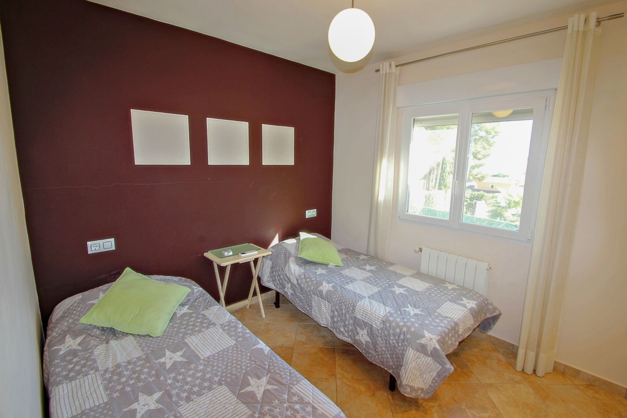 A room with two beds, a small table, and a window with curtains.