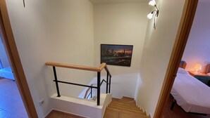 A staircase with a wooden handrail, a cityscape painting on the wall, and a bed with a white cover in the adjacent room. - Daró 3D 37 - A/C, pool and 150m from the beach (Torroella de Montgri)