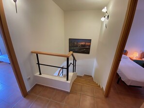 Eine Treppe mit einer Holzhandläufe, ein Stadtbildgemälde an der Wand und ein Bett mit weißer Bettdecke im angrenzenden Zimmer.