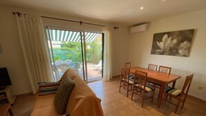 A living room with a sofa, a dining table with chairs, a TV, and a sliding glass door leading to an outdoor area with a patio and chairs. - Daró 3D 37 - A/C, pool and 150m from the beach (Torroella de Montgri)