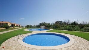 A swimming pool with a stone deck, surrounded by a well-maintained lawn and a few houses in the background. - Daró 3D 37 - A/C, pool and 150m from the beach (Torroella de Montgri)