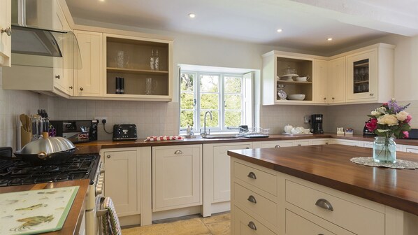 A kitchen with white cabinets, a wooden countertop, a stove, and a window with a view of greenery. - A sudeley castle cottage that sleeps 14 guests  in 7 bedrooms (Winchcombe)