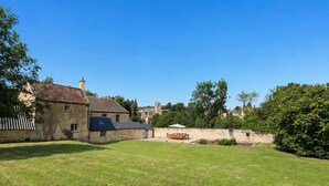 A stone building with a sloped roof, a grassy yard, and a distant view of a church tower.
