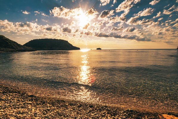 A clear view of a beach with pebbles and calm water reflecting the sun.
