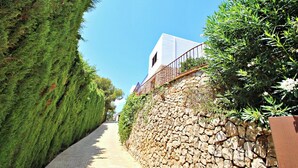 A narrow stone pathway flanked by dense green shrubbery and a stone wall. - Argentario - sea view villa with private pool in Benissa (Benissa)