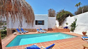 A rectangular pool with blue and white lounge chairs, a thatched umbrella, and a white building with a window. - Argentario - sea view villa with private pool in Benissa (Benissa)